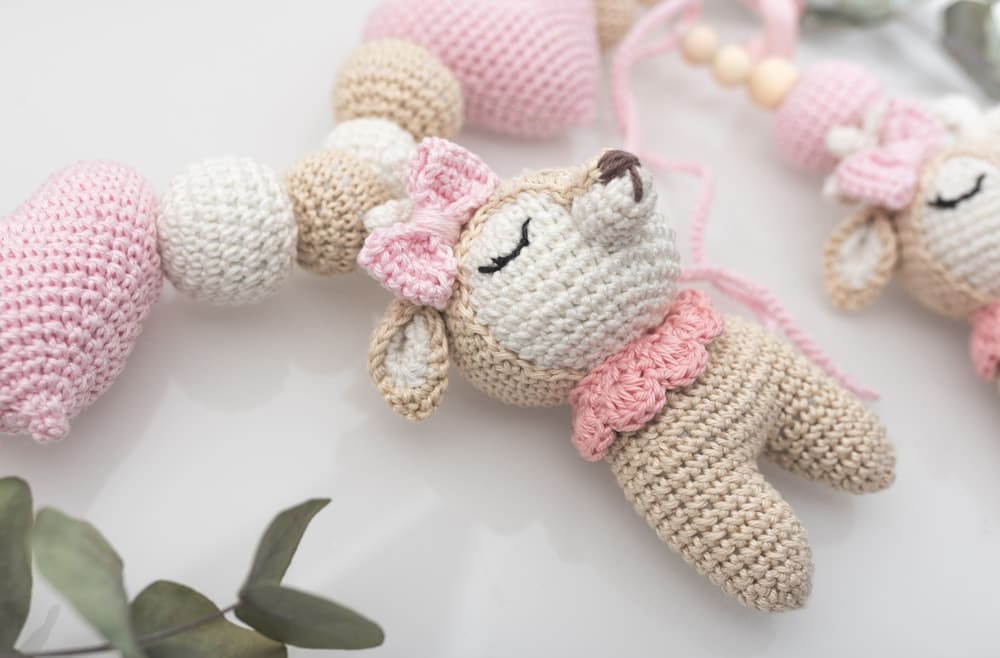 A pink and cream crocheted amigurumi bear with a bow