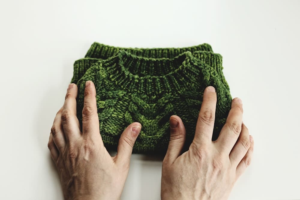 Two hands holding a folded forest green cable-knit piece